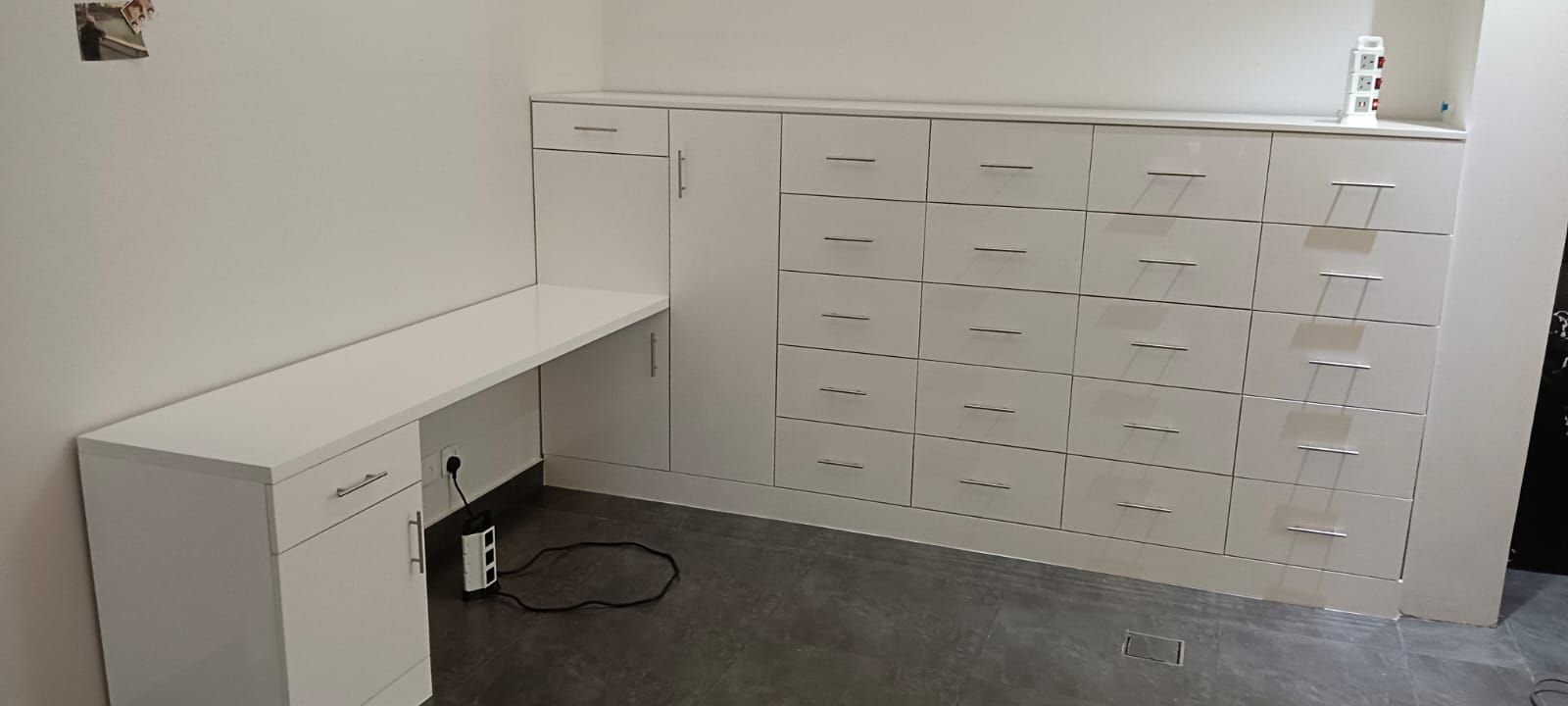 A space-maximizing bedroom installation featuring a floating corner study desk smoothly transitioning into a full-height wardrobe system equipped with multi-tier square drawer units. - Photo 1
