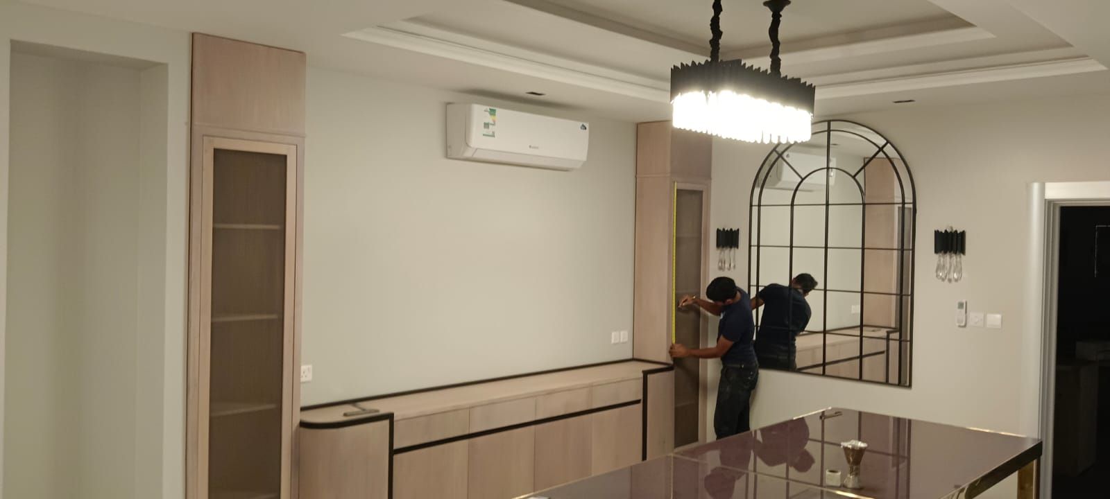 وحدة طعام مدمجة مخصصة ممتدة من الأرض إلى السقف، تتكون من خزانتين طويليتين بجوانب وأبواب زجاجية تحيطان بكاونتر بوفيه منخفض يحتوي على أدراج مدمجة وأطراف داكنة مميزة. - صورة 1