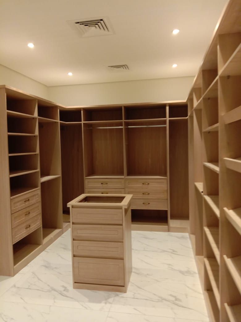 A luxury wrap-around walk-in wardrobe system covering three complete walls with custom cabinetry, integrated display shelving, glass-front cupboards, and a large matching central storage island. - Photo 1