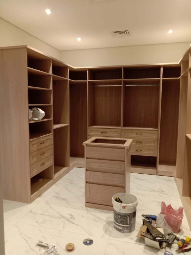 A luxury wrap-around walk-in wardrobe system covering three complete walls with custom cabinetry, integrated display shelving, glass-front cupboards, and a large matching central storage island. - Photo 2