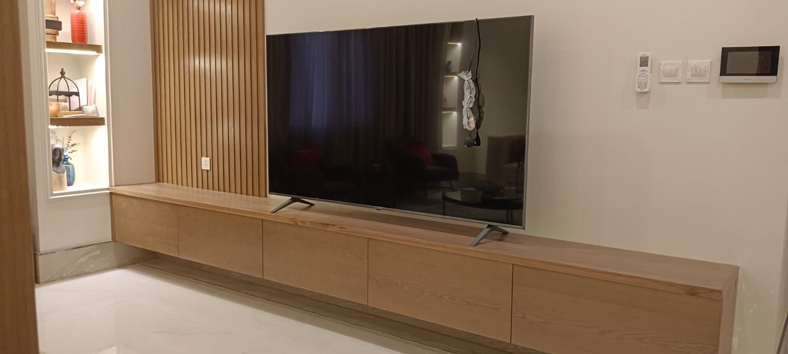 A minimalist wall-mounted television back panel assembly integrated with a low-profile floating media shelf underneath and a matching vertical open-shelf unit tucked into the corner. - Photo 1