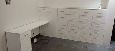 A space-maximizing bedroom installation featuring a floating corner study desk smoothly transitioning into a full-height wardrobe system equipped with multi-tier square drawer units.