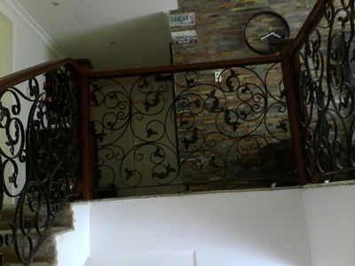 Premium interior staircase woodwork featuring a smooth, contoured wooden handrail mounted on top of iron balusters, anchored by solid wooden newel posts with decorative turned detailing.