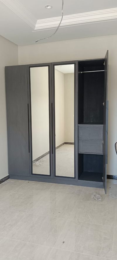 A modern, floor-to-ceiling built-in wardrobe featuring a textured dark grey finish, long minimalist black handles, integrated full-length mirrors, and an organized internal layout with shelving and hanging rods.