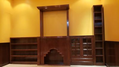 A classic dark-finished wood wall assembly featuring a central fireplace mantel with an overmantel frame, flanked by asymmetrical storage including an open bookcase shelf, a small cabinet with decorative leaded glass doors, and integrated upper shelving units.