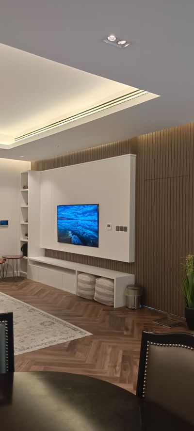A modern living room entertainment unit featuring a wood veneer TV mounting panel, a low-profile floor media console with open components, and an integrated tall vertical shelving unit on the left.